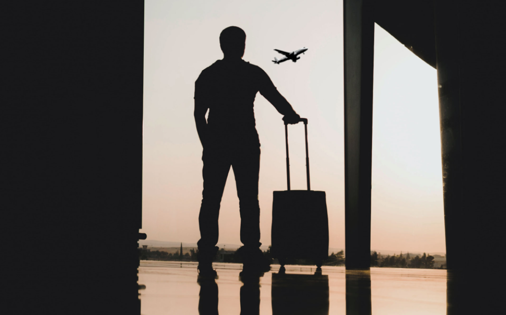 Pessoa com mala em aeroporto ao entardecer, simbolizando planejamento e organização para viagens.