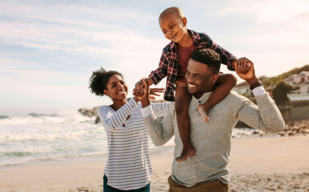família com pai, mãe e filho nos ombros do pai caminham pela praia durante sua viagem de carro