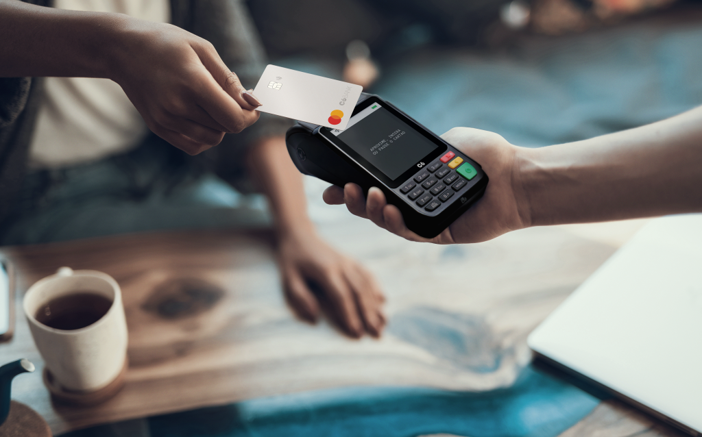 um cartão do C6 Bank sendo utilizado para efetuar um pagamento por aproximação em uma maquininha C6 Pay.