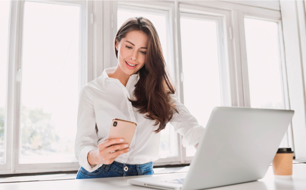 Mulher mexendo no celular para pegar o Apple Pay e pagar as compras no computadolr