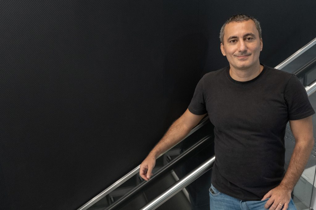 Felipe Salles, Head de Economia do C6 Bank, em pé em um dos andares do banco. Ele usa uma camiseta preta e uma calça jeans.