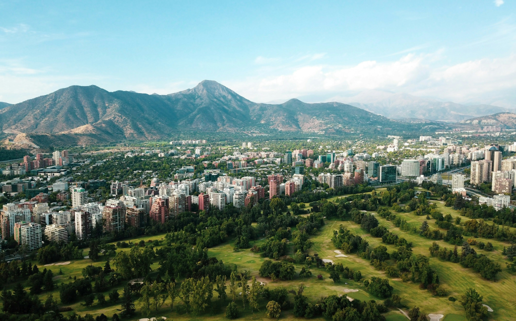 Vista aérea da cidade de Santiago, Chile, com prédios residenciais e área verde. Montanhas ao fundo complementam a paisagem urbana.