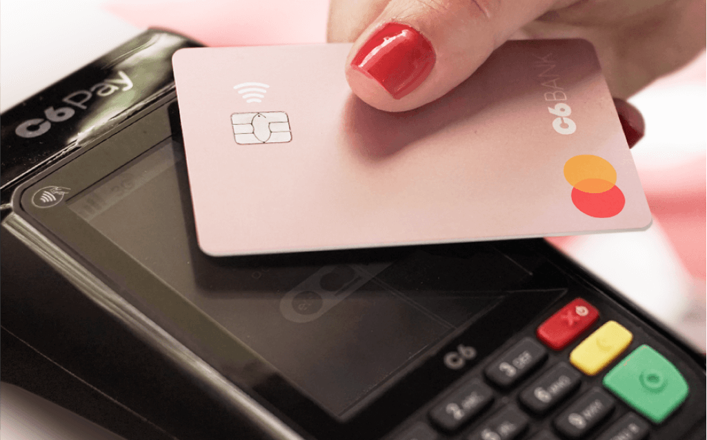Pessoa utilizando cartão do C6 Bank em maquininha de pagamento C6 Pay para transação financeira rápida e segura.