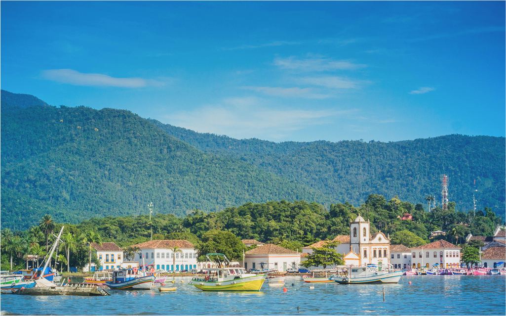 Vista panorâmica de um lindo porto com barcos coloridos, cercado por montanhas e um céu azul claro. Ideal para quem busca natureza e tranquilidade.