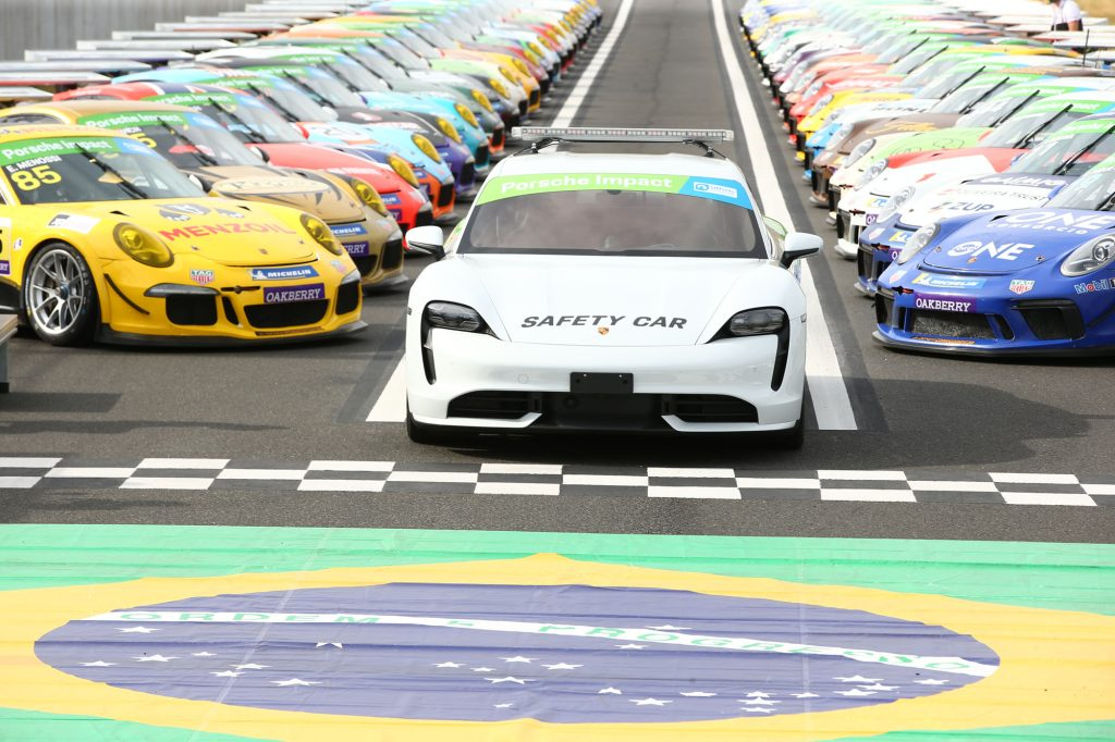 Foto de vários carros alinhados na pista do autódromo de Interlago com um carro da organização à frente e a bandeira do Brasil.