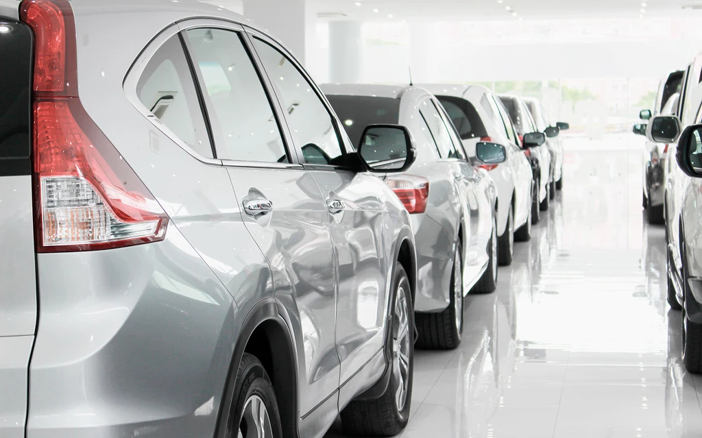 Imagem de um showroom automotivo com vários carros alinhados, destacando um SUV prateado é o foco principal do quadro, ideal para quem busca informações sobre veículos.