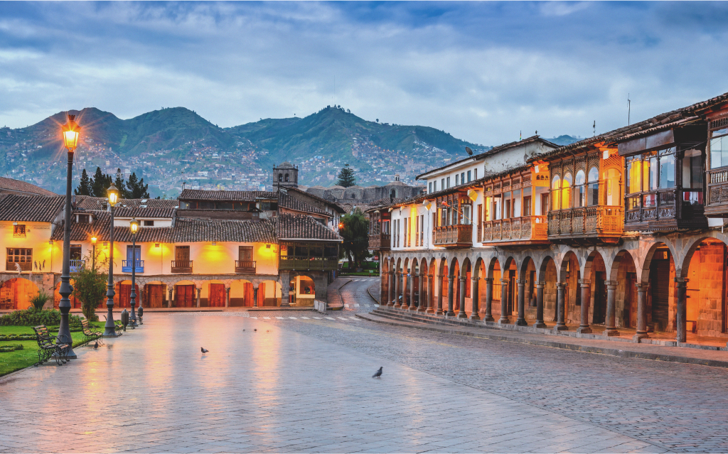 Plaza de Armas em Cusco, Peru, mostrando arquitetura colonial, montanhas ao fundo e iluminação ao entardecer, ideal para turistas.
