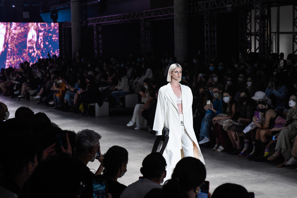 Mulher de conjunto branco e cabelo platinado desfilando na SPFW+, com patrocínio do C6 Bank