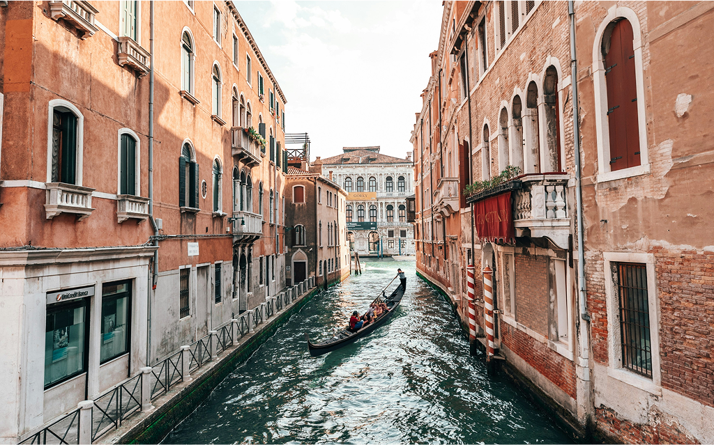 Gôndola navegando por um canal estreito em Veneza, ladeado por edifícios históricos em tons terrosos com varandas e janelas típicas da arquitetura veneziana.