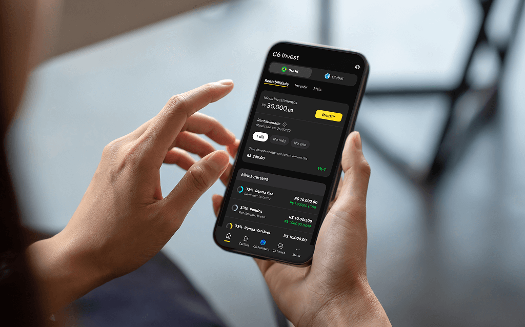 Pessoa segurando um smartphone com o aplicativo C6 Invest aberto na tela. A interface exibe a seção de "Rentabilidade", mostrando um total de R$ 30.000,00 investidos, com detalhes sobre o desempenho no mês e no ano. A carteira está dividida entre renda fixa, fundos de investimento e renda variável, cada um com valor de R$ 10.000,00. O aplicativo tem design escuro e moderno.