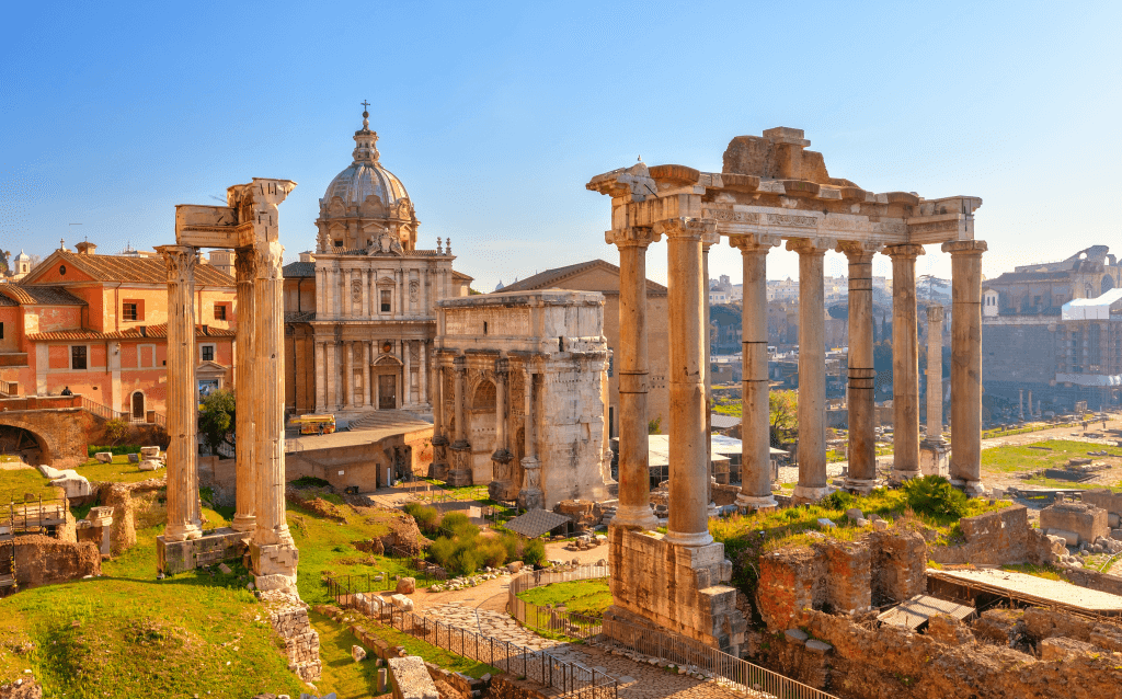 Ruínas do Fórum Romano em Roma iluminadas pela luz dourada do fim de tarde, com colunas coríntias em destaque e a igreja de Santi Luca e Martina ao fundo.