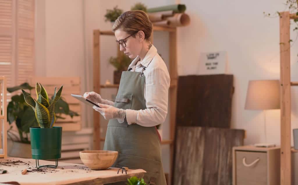 empreendedora branca com cabelo curto e vestindo avental olha para celular e pesquisa o app nota fiscal mei