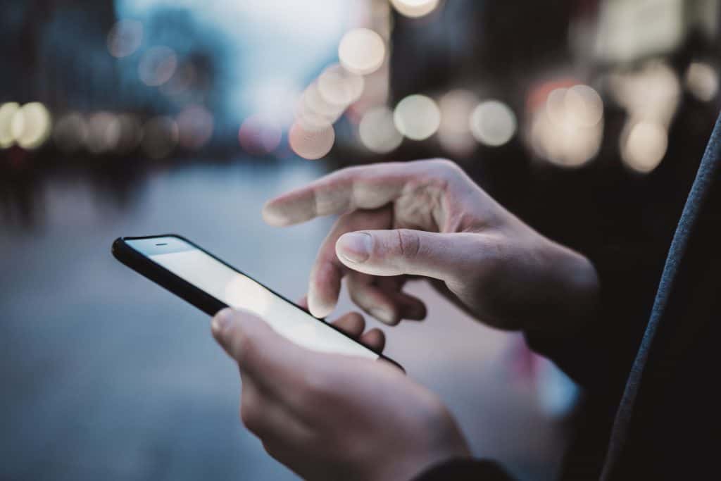 Pessoa usando smartphone em ambiente urbano à noite, com luzes desfocadas ao fundo. Demonstra a importância da tecnologia na vida moderna.