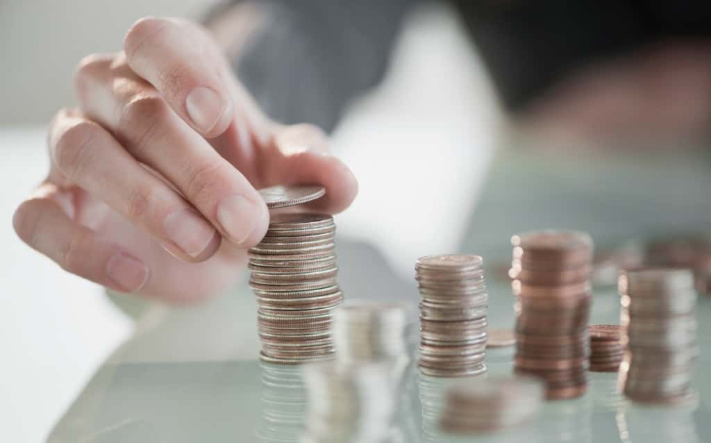 Mão empilhando moedas em pequenas colunas sobre uma mesa, representando a organização financeira e o uso consciente do cheque especial.