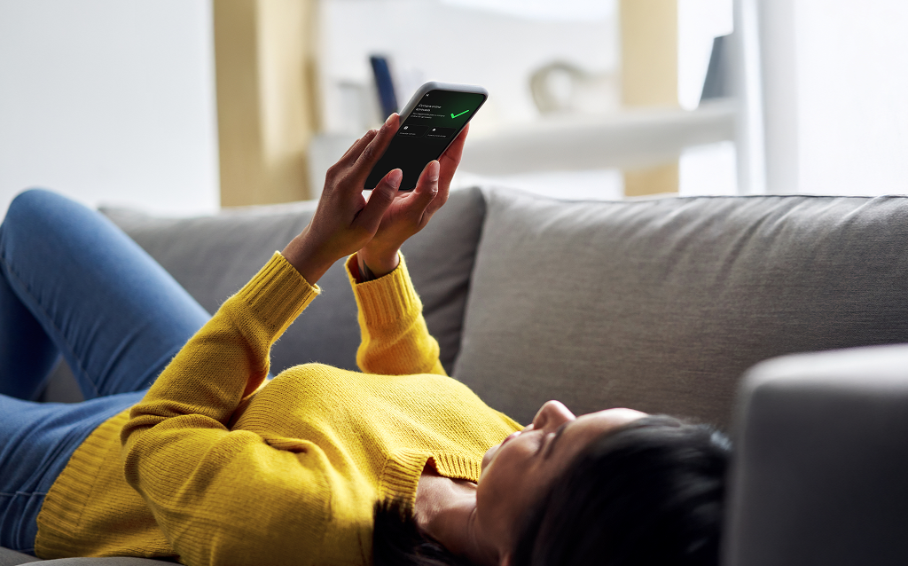Pessoa deitada no sofá usando o celular para ativar o débito automático e organizar suas finanças com praticidade