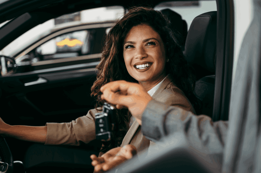Mulher jovem feliz, em um carro, olhando sorrindo para uma pessoa que entrega a ela as chaves do seu carro, representando o início do planejamento de como manter um carro.