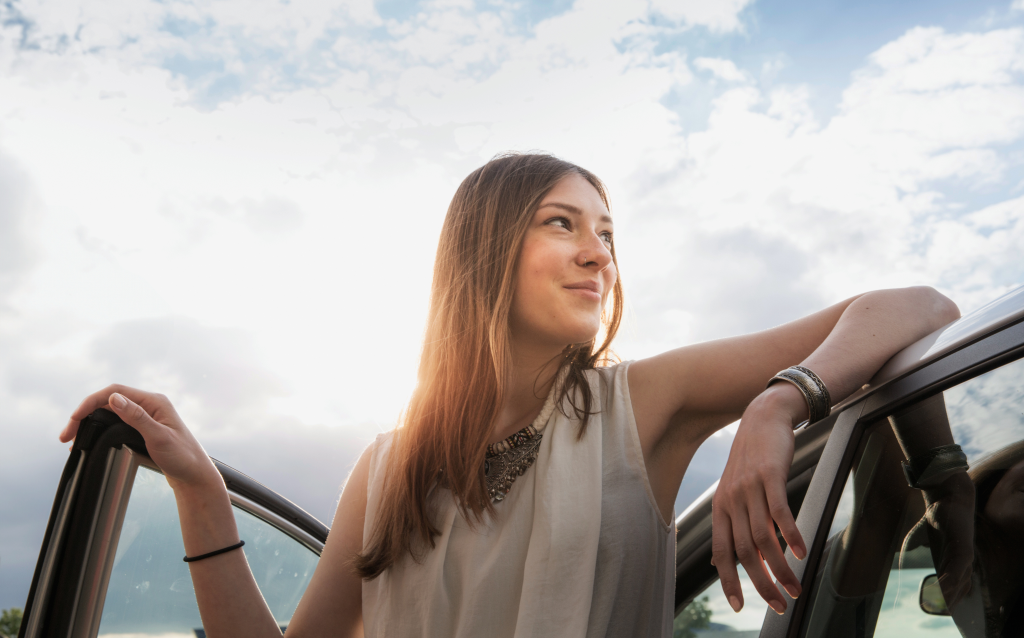 Mulher apoiada na porta do carro
