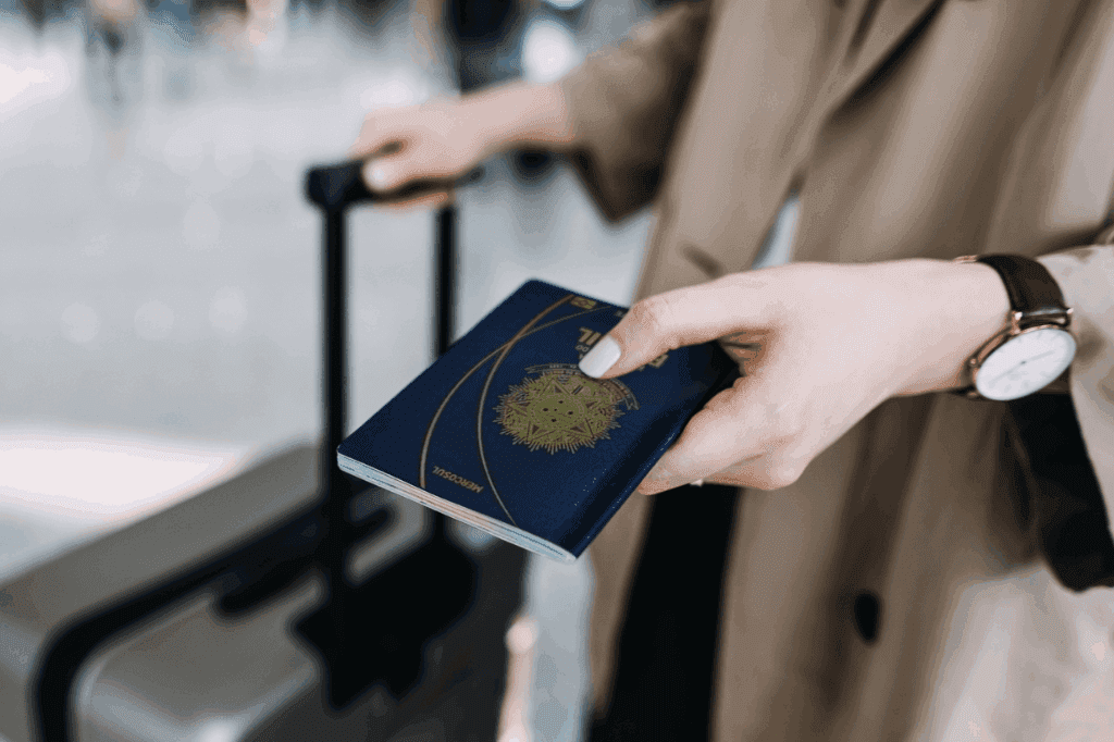 Mãos de uma mulher no aeroporto, segurando a mala e o passaporte, representando o check in e embarque
