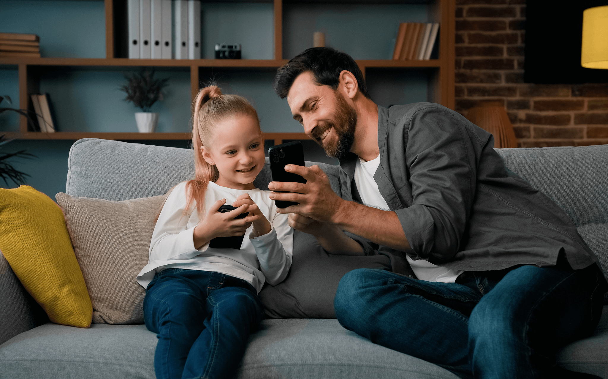 Pai e filha usando celular no sofá de casa, momento de conexão em família.