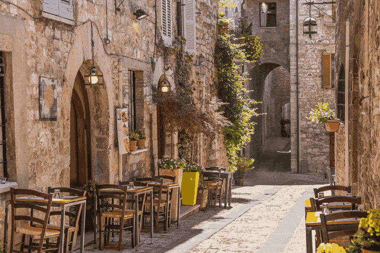 Paisagem de mesas e cadeiras posicionadas em uma rua da Toscana, representando a decisão entre hotel ou pousada.