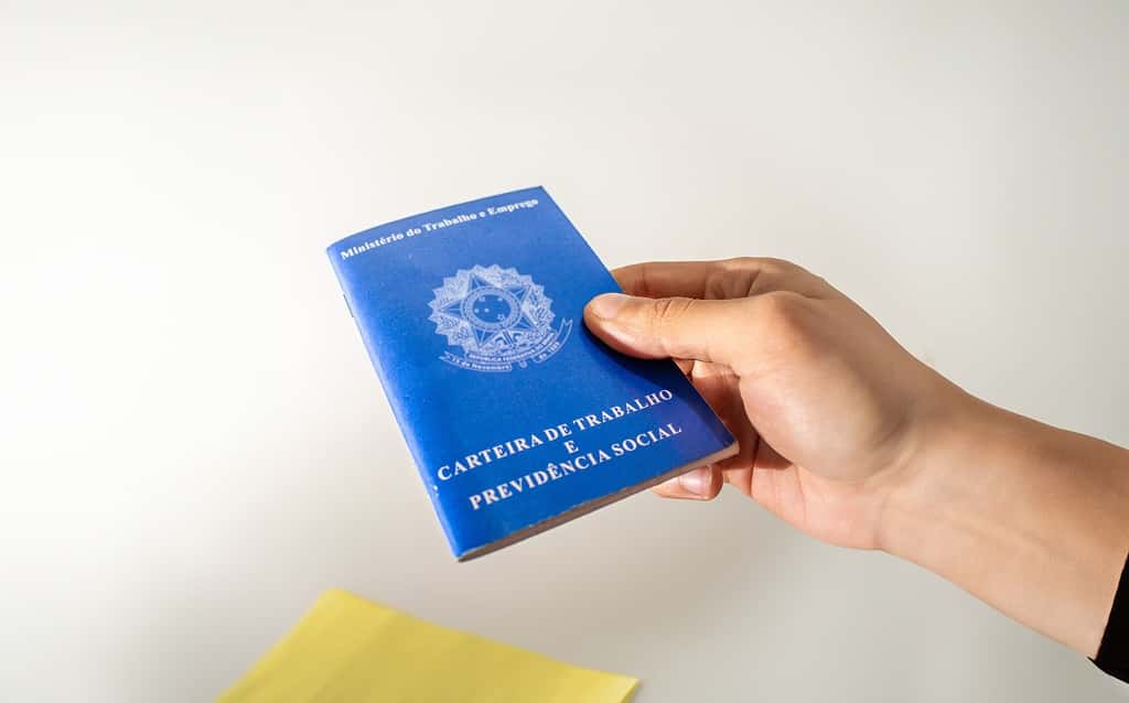 Mão segurando uma Carteira de Trabalho e Previdência Social em fundo neutro, representando vínculos empregatícios e direitos trabalhistas no Brasil.