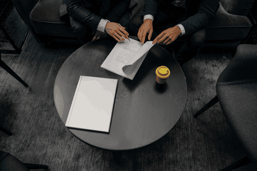 Folhas de um contrato de refinanciamento sobre uma mesa preta, visto de cima. As mãos de dois homens de terno aparecem movimentando os papéis.