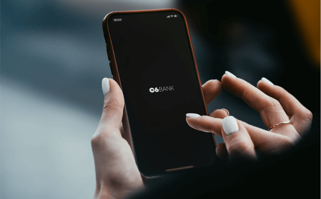 Pessoa segurando um smartphone com a tela exibindo o logotipo do C6 Bank em fundo preto.
