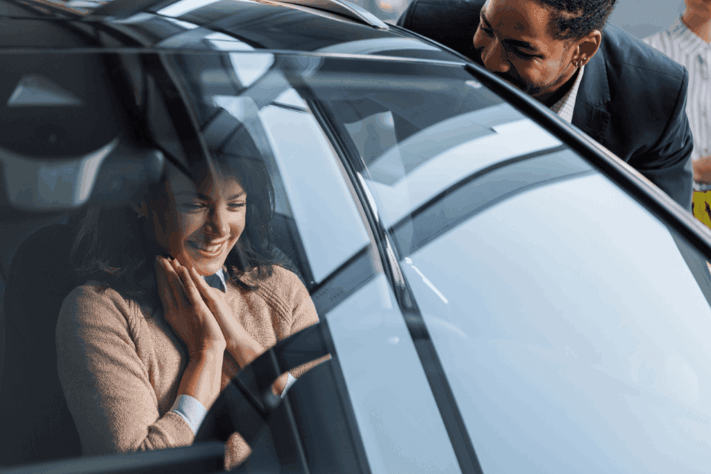 Mulher contente, sorrindo dentro do carro, enquanto um vendedor também sorrindo interage com ela do lado de fora, representando a escolha entre SUV ou sedan