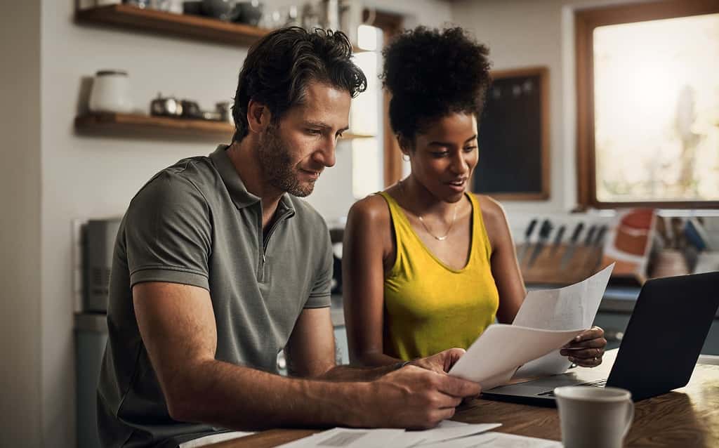 Homem e mulher segurando papeis enquanto analisam se pegam um empréstimo ou consorcio.