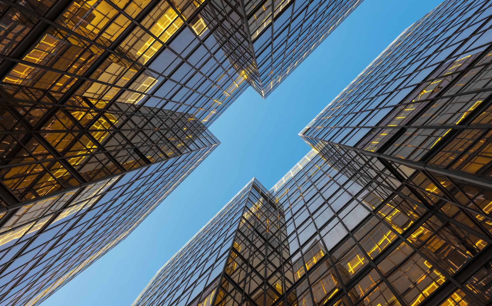 Vista de baixo para cima de prédios corporativos com fachadas de vidro refletindo o céu azul, simbolizando estrutura empresarial e capital social integralizado.