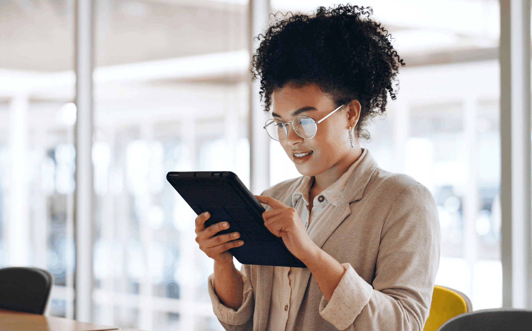 Mulher negra, de óculos e roupa social, em ambiente corporativo iluminado, com dispositivo móvel em mãos, representando uma profissional se informando sobre o empréstimo consignado CLT.