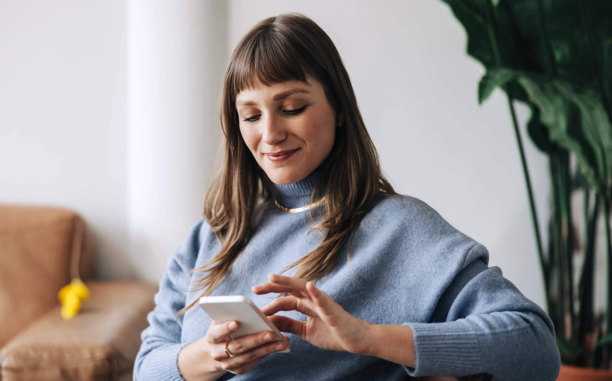 Mulher sentada em ambiente residencial utilizando o celular, representando consulta ou acompanhamento de informações financeiras relacionadas a PEP (Pessoa Politicamente Exposta).