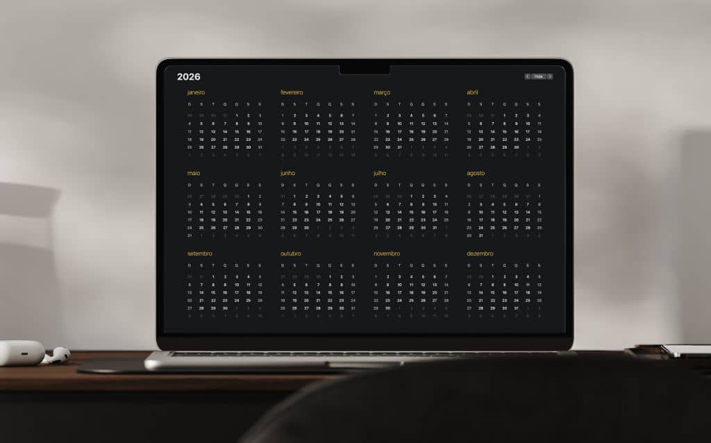 Tela de notebook exibindo um calendário anual de 2026 em fundo escuro, com todos os meses organizados em grade e o notebook apoiado sobre uma mesa em ambiente minimalista.