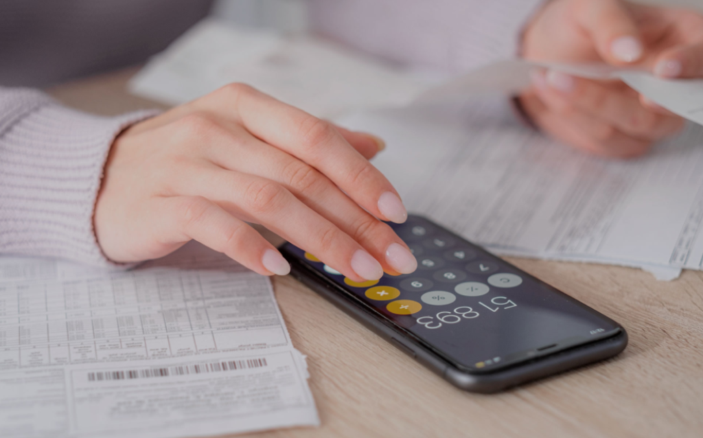 Mão feminina fazendo um cálculo na calculadora do celular relacionado à restituição do Imposto de Renda