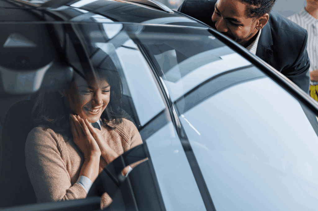 Mulher contente, sorrindo dentro do carro, enquanto um vendedor também sorrindo interage com ela do lado de fora, representando a escolha entre SUV ou sedan