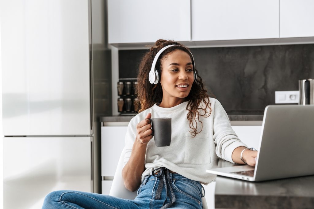 Mulher negra segurando uma xicara, ouvindo música no fone, pesquisando no computador como emitir segunda via Elektro