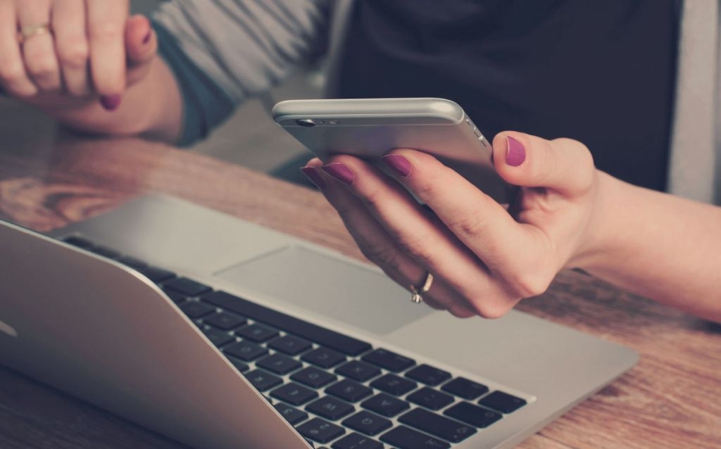 como funciona a portabilidade de salário | mãos delicadas com as unhas pintadas em roxo segurando um celular iphone em frente a um notebook
