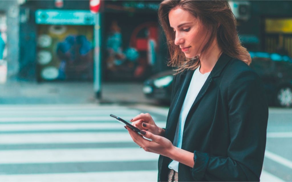 como pagar por aproximação pelo celular - mulher mexendo no celular no meio da rua