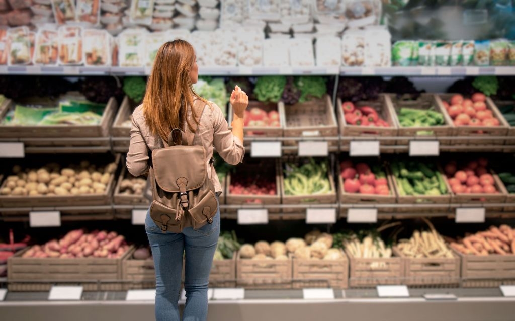 compras de fim ano | mulher loira de cabelos longos parada em frente a diferentes tipos de vegetais em um mercado