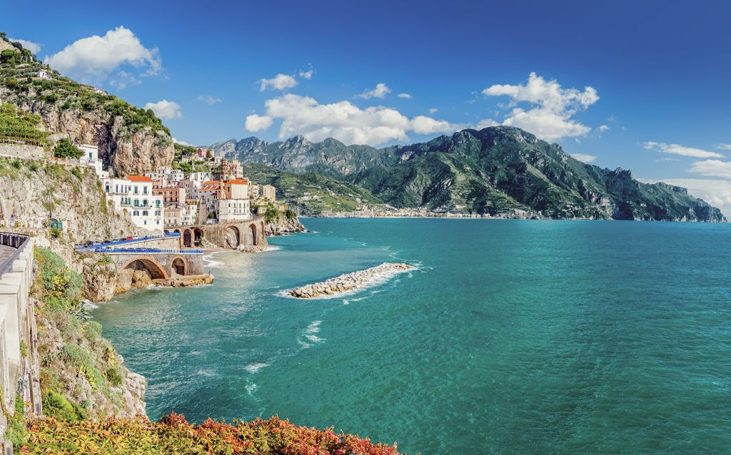 costa amalfitana | praia com águas cristalinas, montanhas ao fundo e um céu bem azul