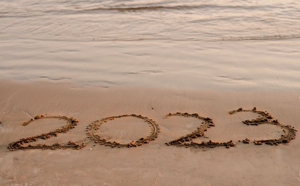 ano 2023 desenhado na areia da praia, ondas ao fundo