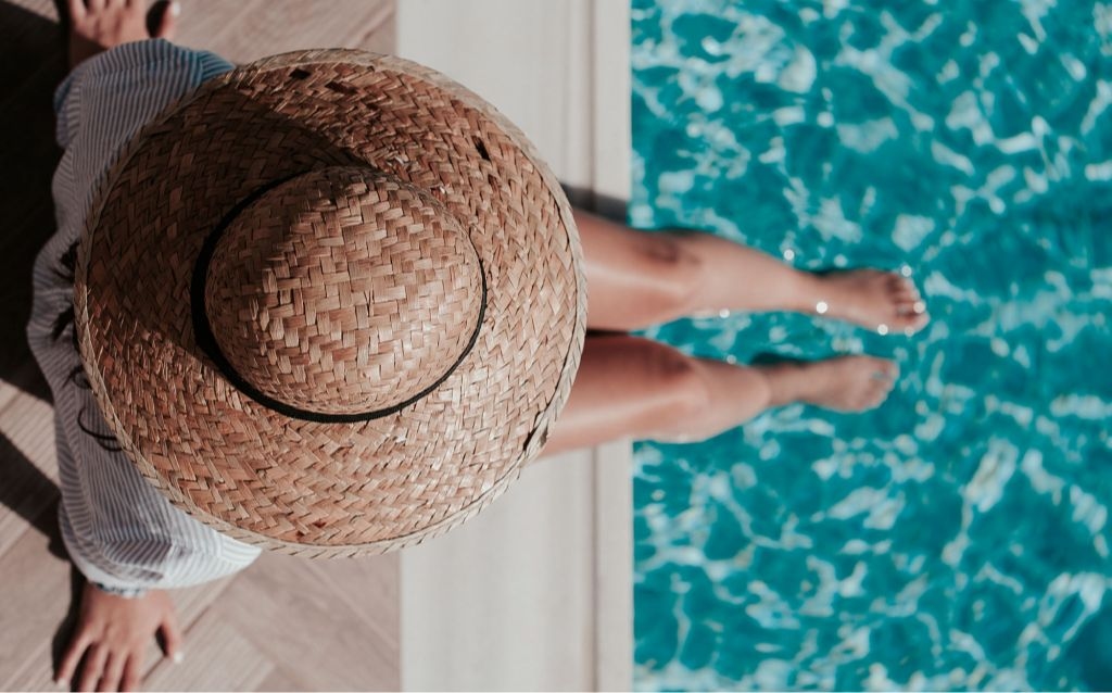 férias de julho | mulher com chapéu de palha e camiseta listrada com pés na piscina em um dia ensolorado