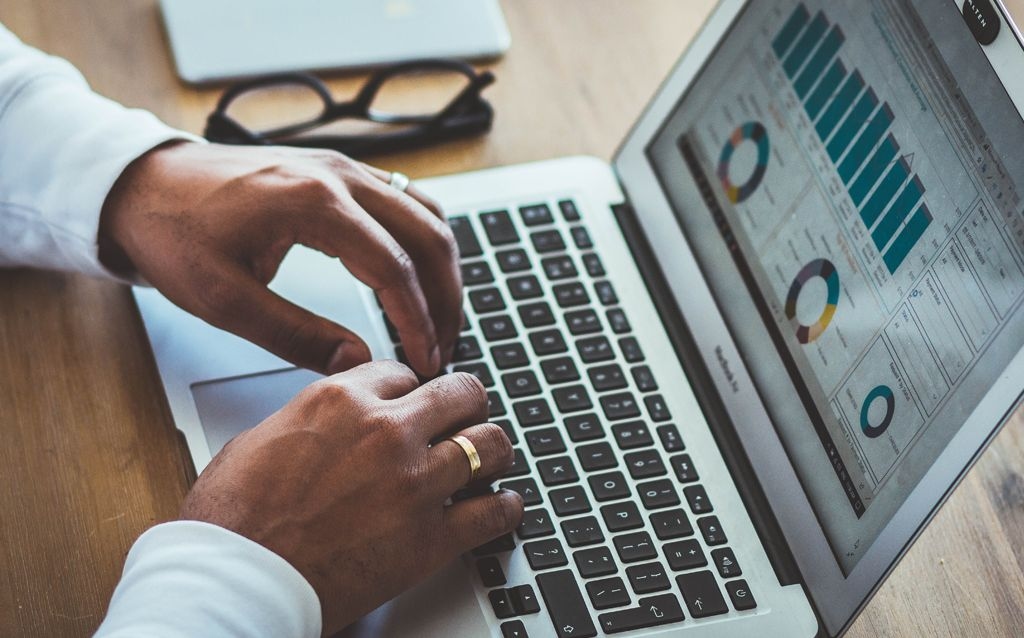 funcionamento holding familiar mãos de um homem negro com uma aliança de casamento digitando em um notebook, na tela gráficos em círculos e em barra