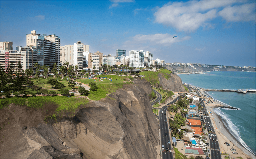 Imagem de uma cidade em cima de uma montanha. Abaixo dela é possível ver estradas o mar de Lima.