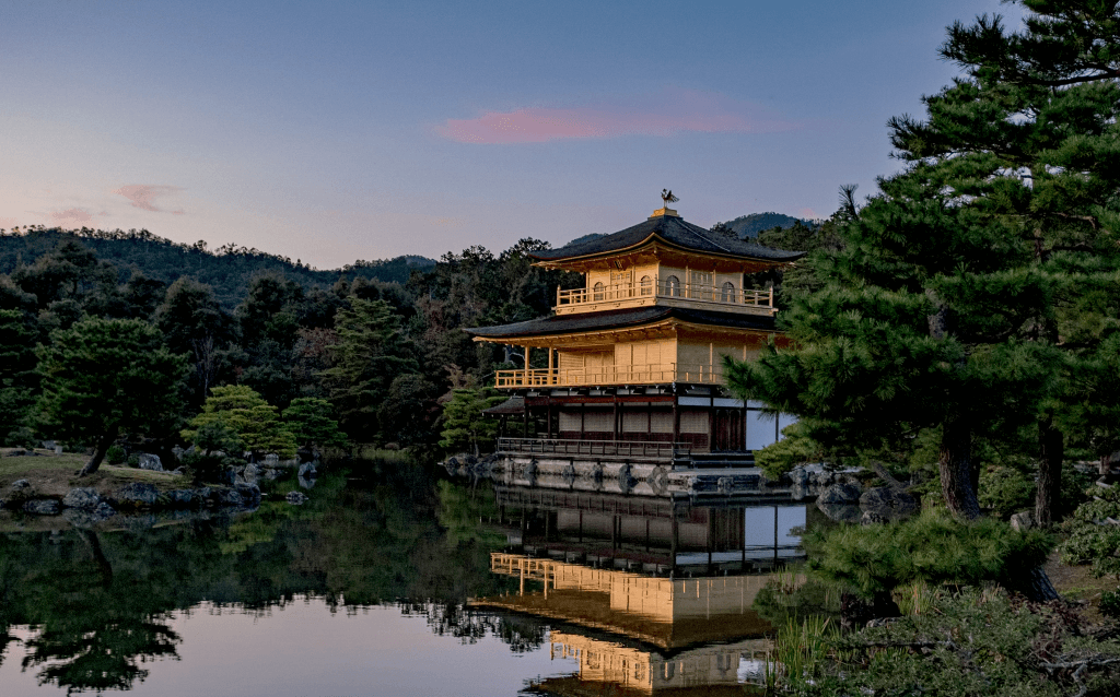 No meio da imagem tem a construção do Templo do Pavilhão Dourado, cercado por árvores e acima de um lago.