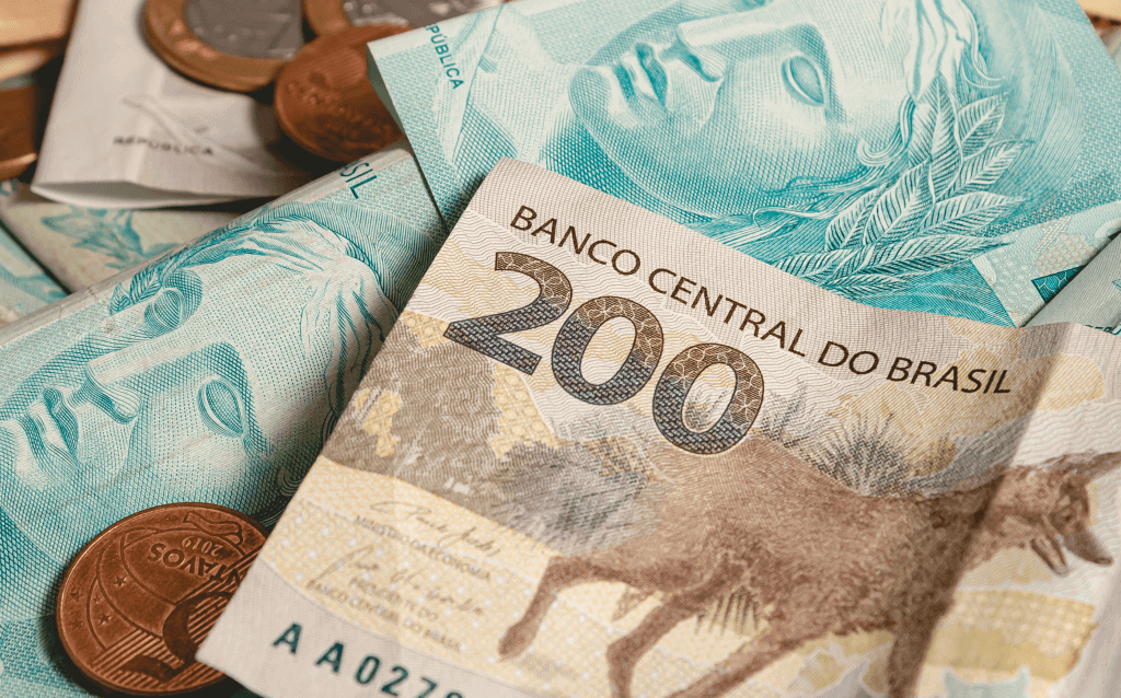 cédulas de 100 e 200 reais espalhadas junto a algumas moedas de um e cinco centavos, a nota de 200 reais está em destaque. o montante simbolizando o valor recebido de PLR