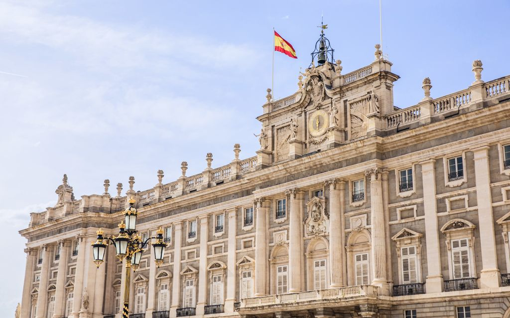 palácio real madrid | edifício com estilo arquitetônico barroco, no topo do palácio tem uma bandeira da espanha
