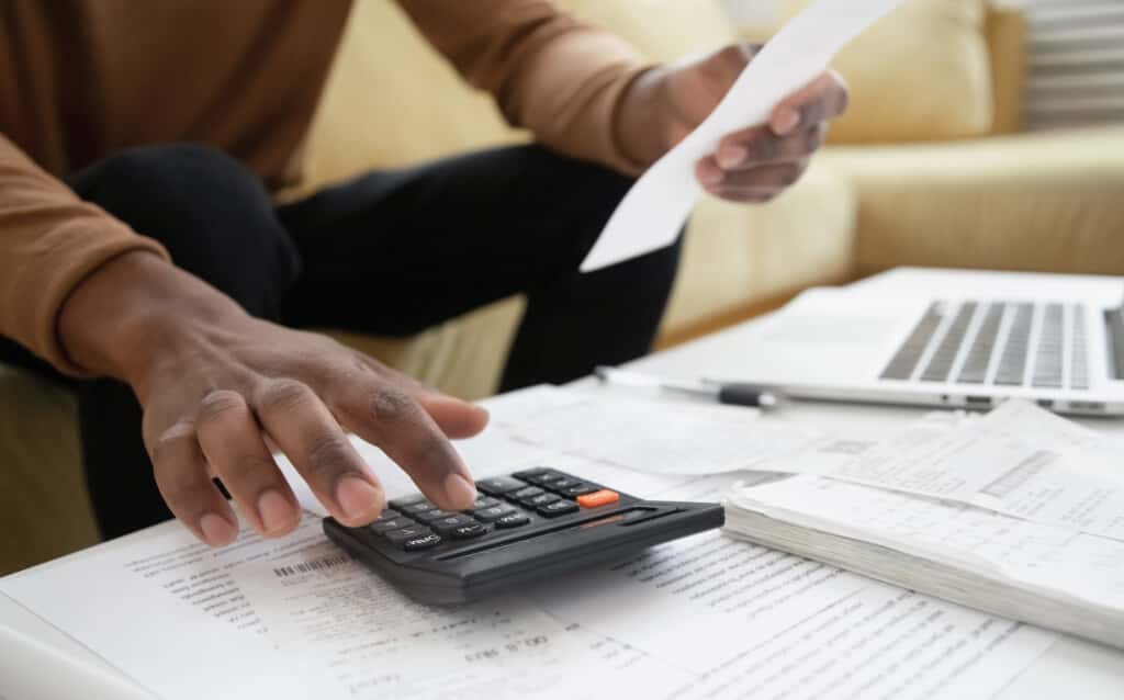 Pessoa de pele negra usando uma calculadora com a mão esquerda e segurando uma folha com a mão direita para ilustrar como declarar fgts no imposto de renda