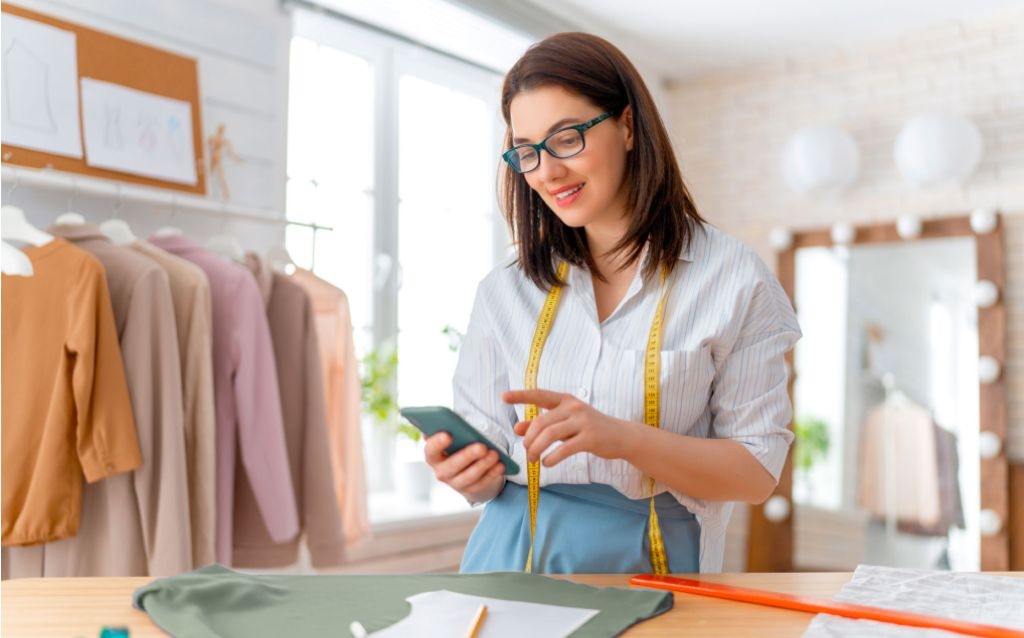 pis e cofins vendedora em uma loja de roupa chique segurando um celular com NFC