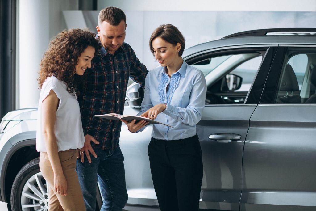 Mulher ao lado de um casal mostrando o manual de um carro